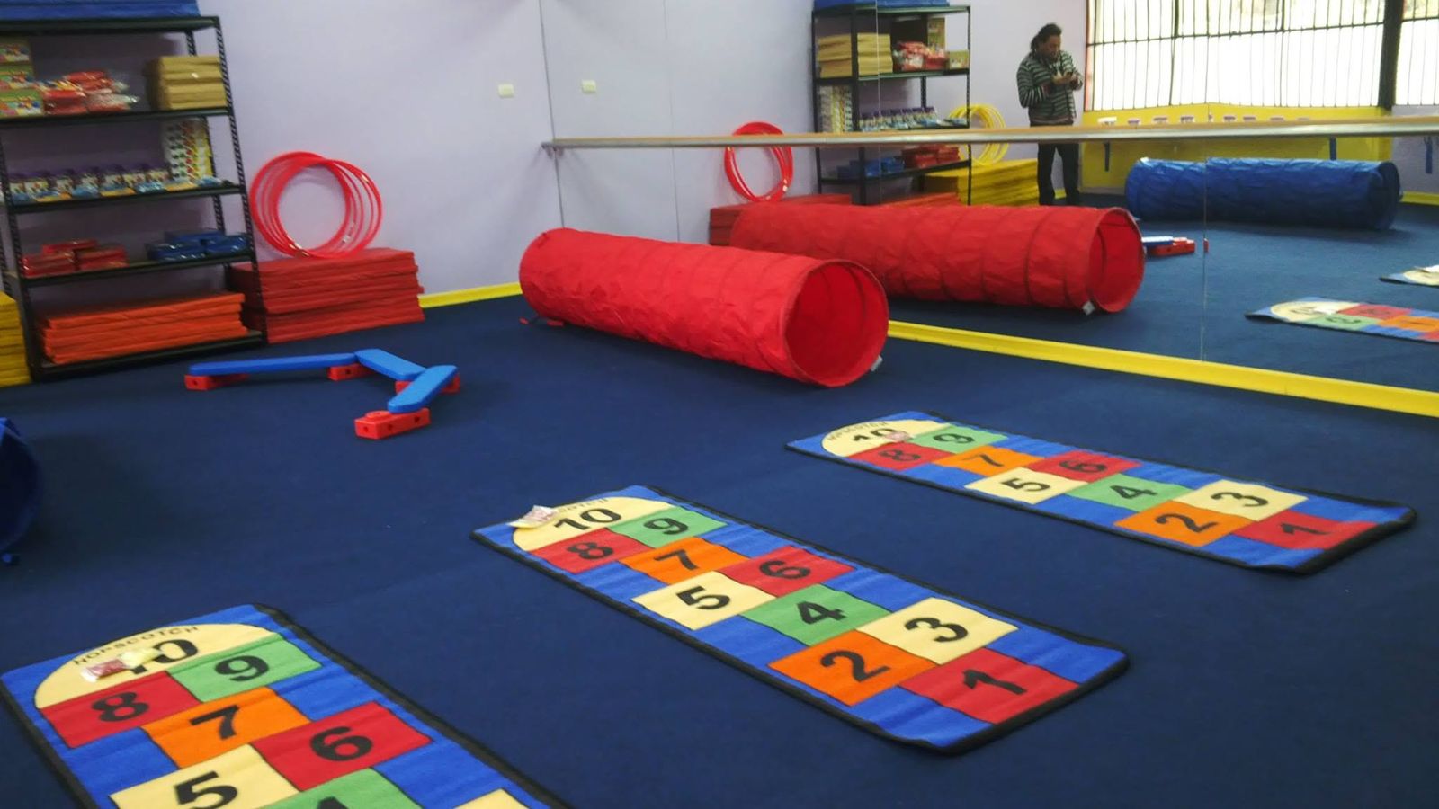 Sala con alfombra azul, alfombras de luche numeradas y túneles rojos