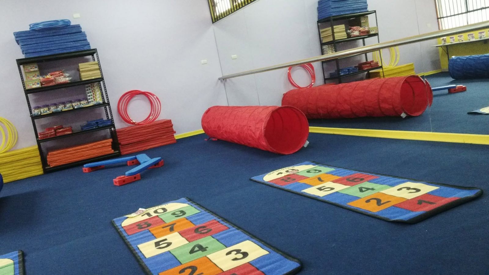 Estanterías con material, colchonetas, aros y túneles sobre alfombra azul